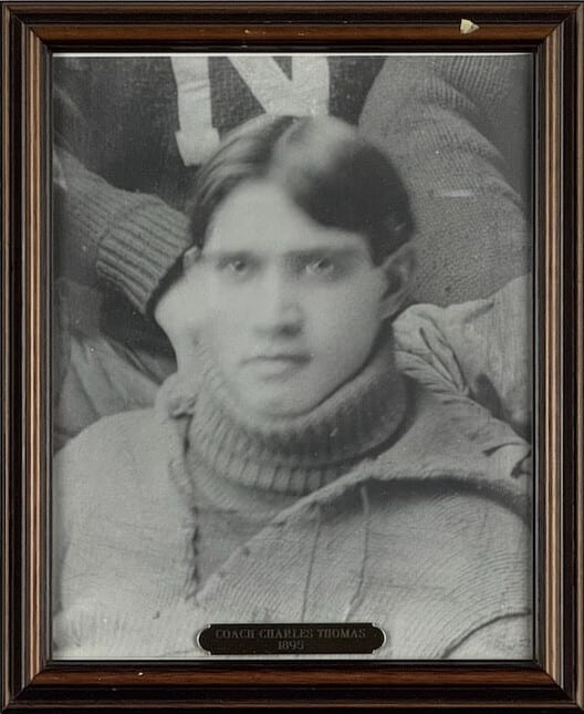 Black-and-white portrait of Charles Thomas in a roll-neck sweater, players crowded behind him.