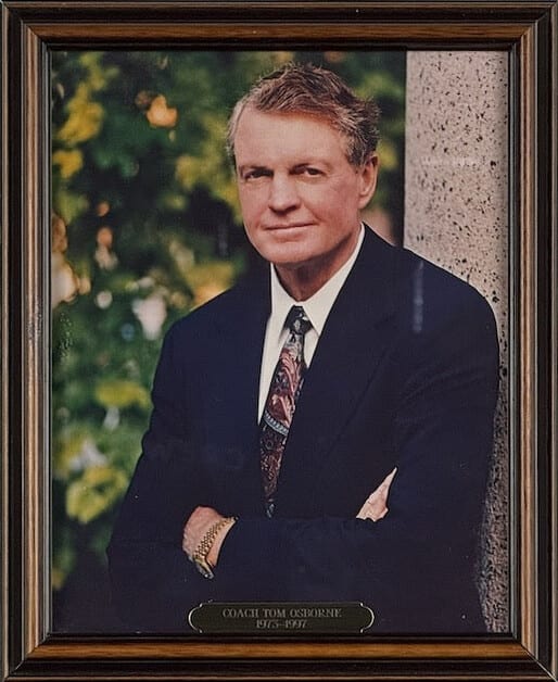 Colour portrait of Tom Osborne, arms folded, in a navy suit beside a stone column.