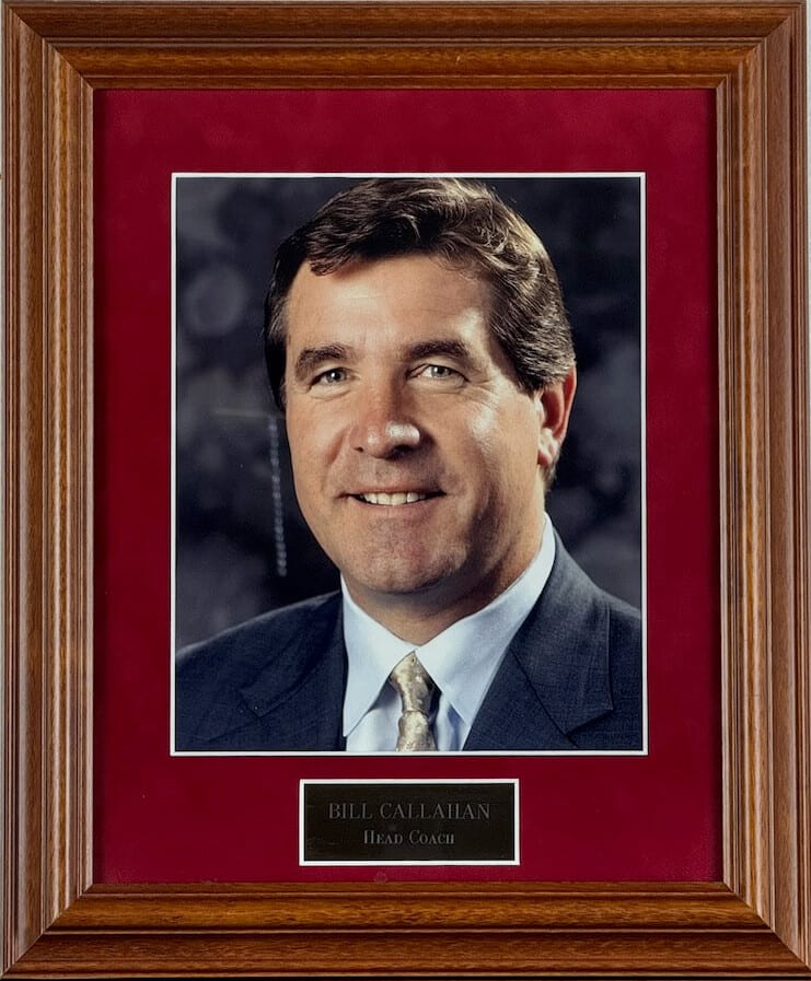 Colour portrait of Bill Callahan, smiling, on a red mat in a larger oak frame with a brass plate reading Head Coach.